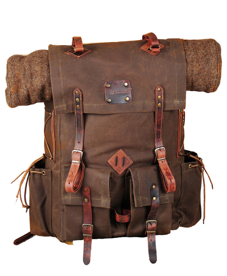 May include: A brown canvas backpack with leather straps and buckles. The backpack has a large main compartment and two smaller pockets on the front. The backpack is made of durable materials and is perfect for carrying all of your essentials.