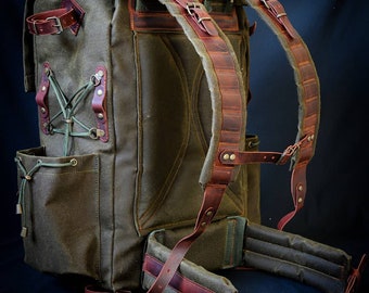 May include: A large, green canvas backpack with brown leather straps and buckles. The backpack has a large main compartment and several smaller pockets.