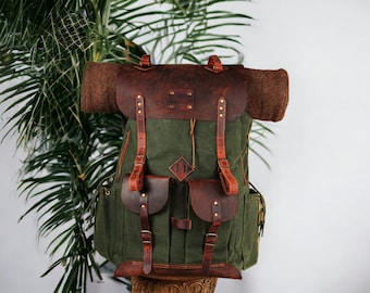 May include: A green canvas backpack with brown leather straps and accents. The backpack has two large pockets on the front and a smaller pocket on the top.