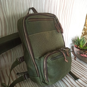 May include: A green canvas backpack with brown leather accents and multiple zipped compartments. The backpack has adjustable straps and a padded back panel.