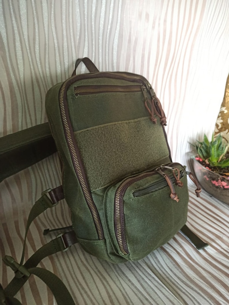 May include: A green canvas backpack with brown leather accents and multiple zipped compartments. The backpack has adjustable straps and a padded back panel.