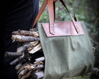 May include: A green canvas bag with brown leather handles and trim. The bag is filled with sticks of firewood.