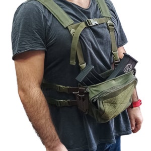 May include: A green tactical chest rig with a large pouch and two magazine holders. The rig has adjustable straps and is worn over a grey t-shirt.