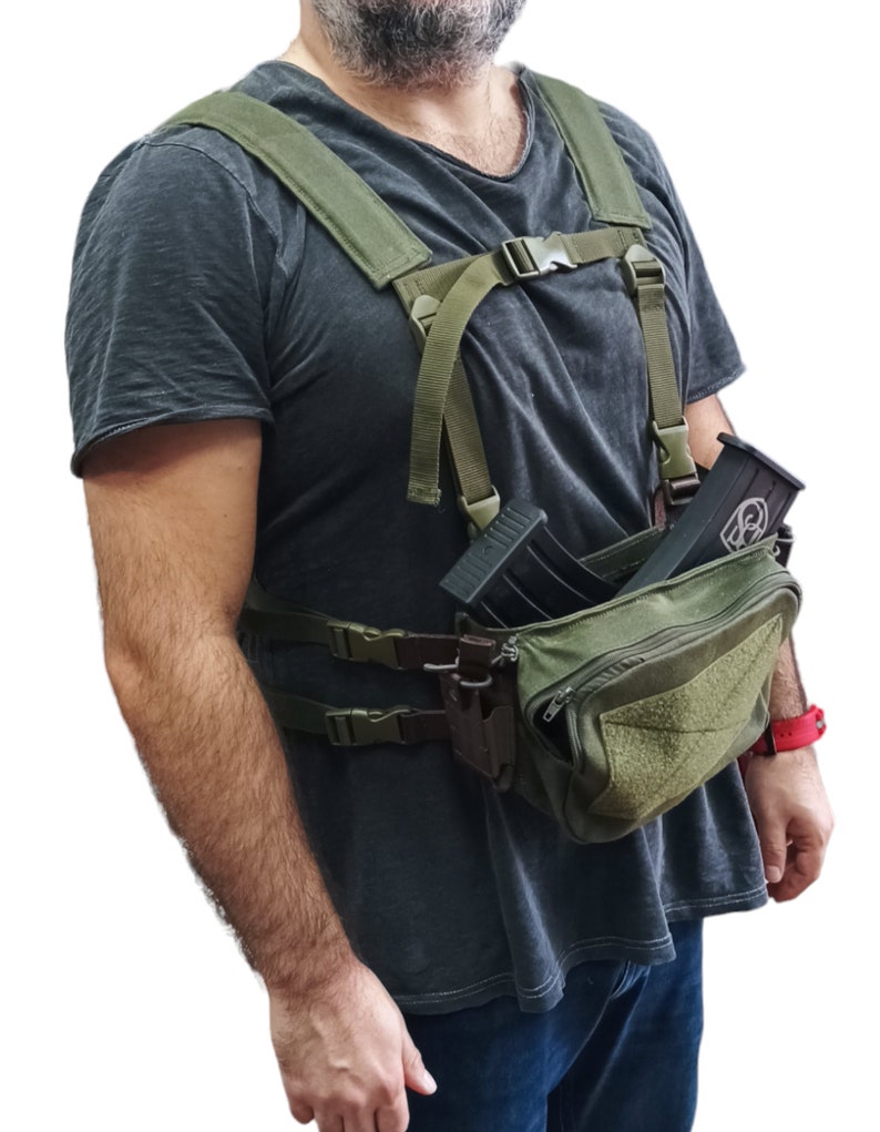 May include: A green tactical chest rig with a large pouch and two magazine holders. The rig has adjustable straps and is worn over a grey t-shirt.