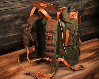 May include: A green canvas backpack with brown leather straps and accents. The backpack has a drawstring closure and a flap with a buckle.
