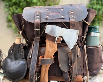 May include: A brown canvas and leather backpack with an axe secured to the front. The backpack has multiple pockets and straps, with a leather canteen and a green insulated bottle on the sides. The axe has a wooden handle and a silver blade.