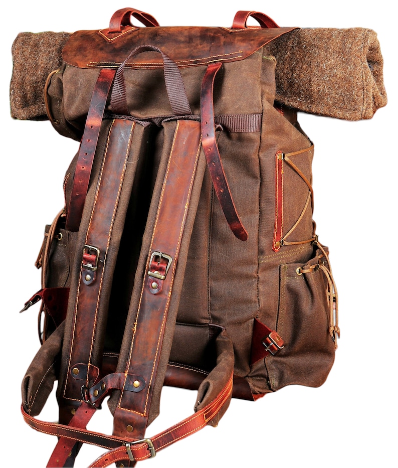 May include: A brown canvas backpack with leather straps and buckles. The backpack has a large main compartment and a smaller front pocket. The backpack is designed for carrying heavy loads.