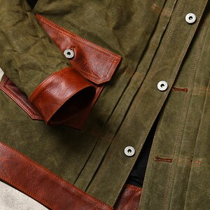 May include: A green canvas jacket with brown leather accents. The jacket has a button closure and two large pockets on the front. The pockets are also trimmed with brown leather.
