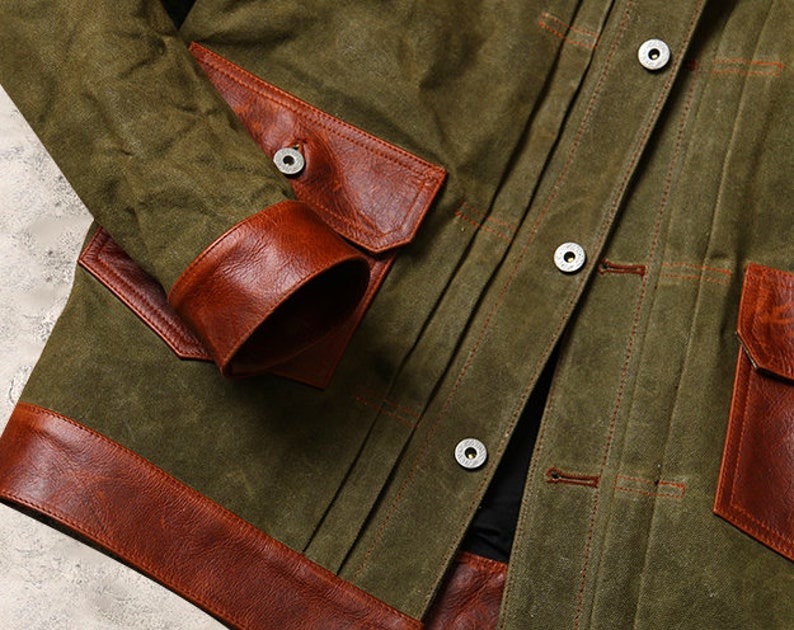 May include: A green canvas jacket with brown leather accents. The jacket has a button closure and two large pockets on the front. The pockets are also trimmed with brown leather.