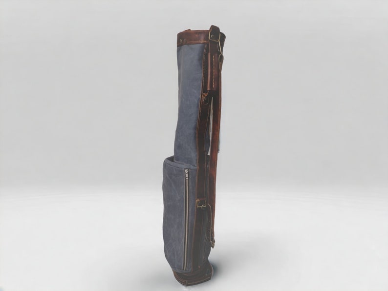 May include: A blue canvas golf bag with brown leather accents and straps. The bag has a zippered pocket on the side.