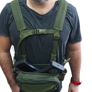May include: A green tactical chest rig with adjustable straps and two magazine pouches. The rig is being worn and has a black magazine inserted in one of the pouches.