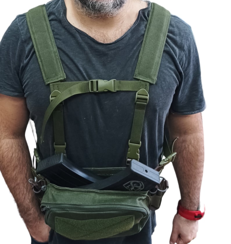 May include: A green tactical chest rig with adjustable straps and two magazine pouches. The rig is being worn and has a black magazine inserted in one of the pouches.