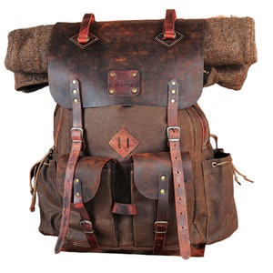 May include: A brown leather and canvas backpack with a large flap and multiple pockets. The backpack has a leather patch with the text "Blackcraft" on it.