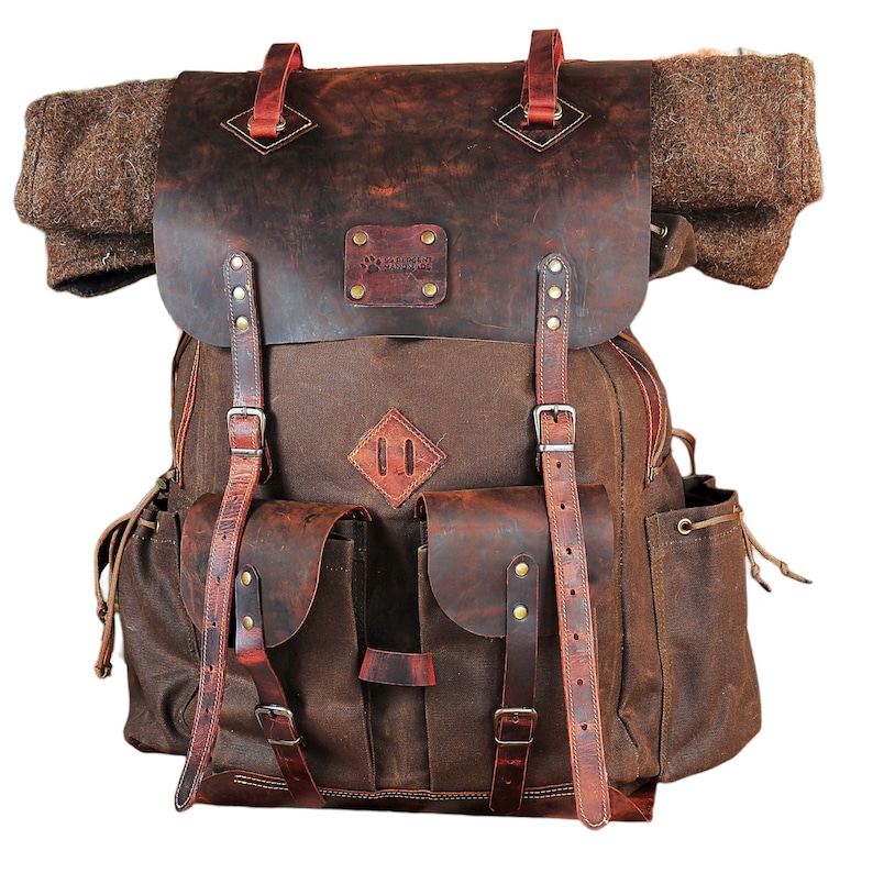 May include: A brown leather and canvas backpack with a large flap and multiple pockets. The backpack has a leather patch with the text "Blackcraft" on it.