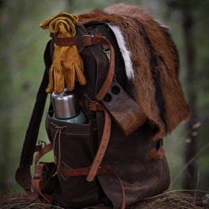 May include: A brown leather backpack with a fur trim, a metal thermos, and a pair of yellow leather gloves. The backpack has multiple straps and buckles.