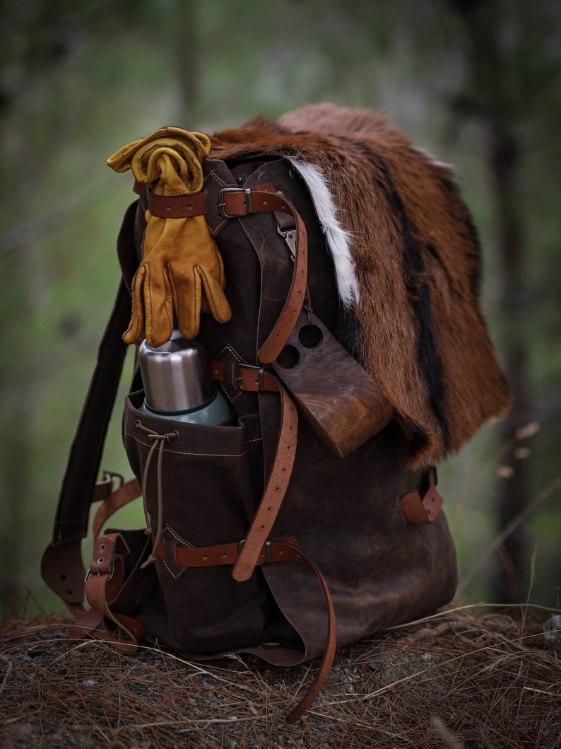 May include: A brown leather backpack with a fur trim, a metal thermos, and a pair of yellow leather gloves. The backpack has multiple straps and buckles.