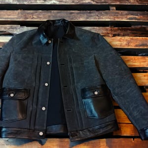 May include: A dark blue denim jacket with black leather trim around the collar, pockets, and bottom hem. The jacket has a button-up front closure and two flap pockets.