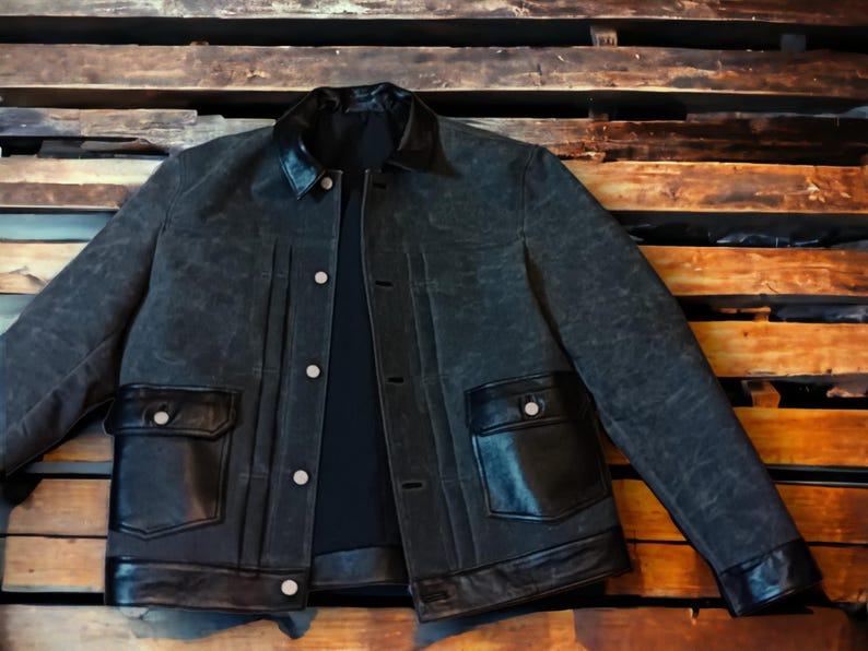 May include: A dark blue denim jacket with black leather trim around the collar, pockets, and bottom hem. The jacket has a button-up front closure and two flap pockets.