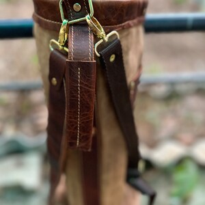 May include: A brown leather golf bag with a canvas body and a brass buckle. The bag has a brown leather strap with a brass buckle.