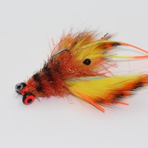 May include: A brown and yellow fly fishing lure with orange and black accents. The lure has a red and black eye.