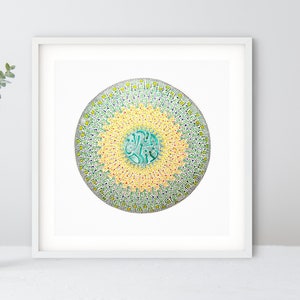 May include: A framed print of a circular mandala design with a green, yellow, and white color scheme. The mandala is surrounded by a white border.