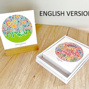 May include: Two versions of a greeting card featuring a circle of colorful flowers and Hebrew text. The card on the left is a white card with the text "Happy Holiday" and the card on the right is a white card with the text "Freedom".
