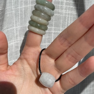 May include: A set of six jade rings stacked on a finger, and a white jade pendant on a black cord.