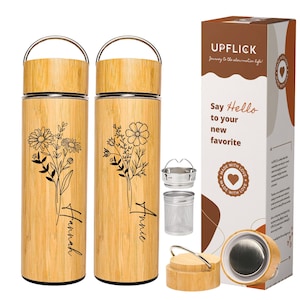 May include: Two bamboo travel mugs with floral designs and personalized names "Hannah" and "Annie". The mugs have a stainless steel interior and come with a stainless steel tea infuser. The mugs are packaged in a brown box with the brand name "Upflick" and the text "Say Hello to your new favorite".