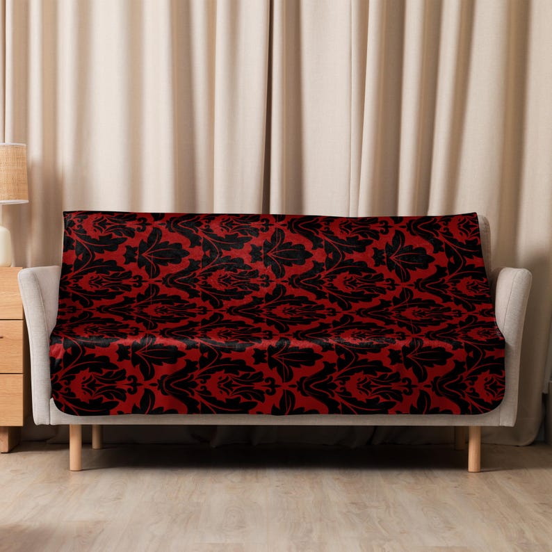 May include: A red and black damask patterned sofa throw blanket. The throw is draped over a sofa with a wooden frame and light brown upholstery.