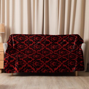 May include: A red and black throw blanket with a damask pattern. The blanket is draped over a couch.