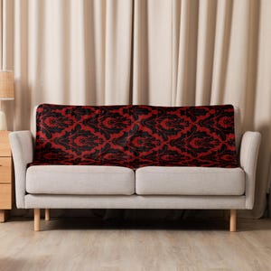 May include: A red and black patterned throw blanket draped over a light gray sofa.
