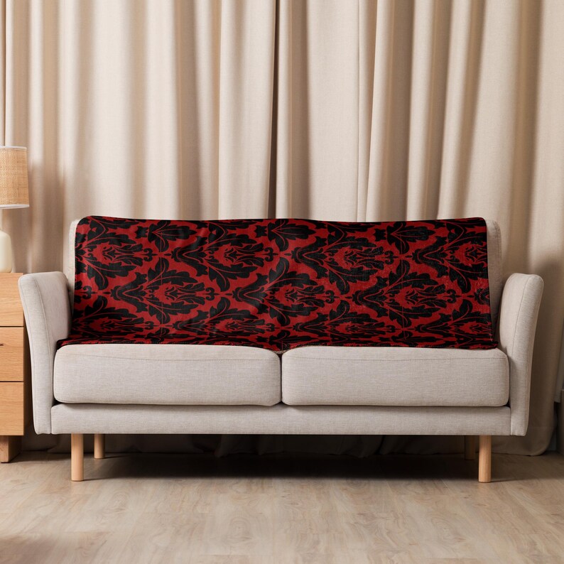 May include: A red and black patterned throw blanket draped over a light gray sofa.
