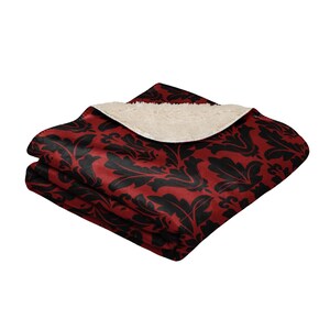 May include: A red and black patterned throw blanket with a soft, white sherpa lining. The blanket is folded in half and the sherpa lining is visible.