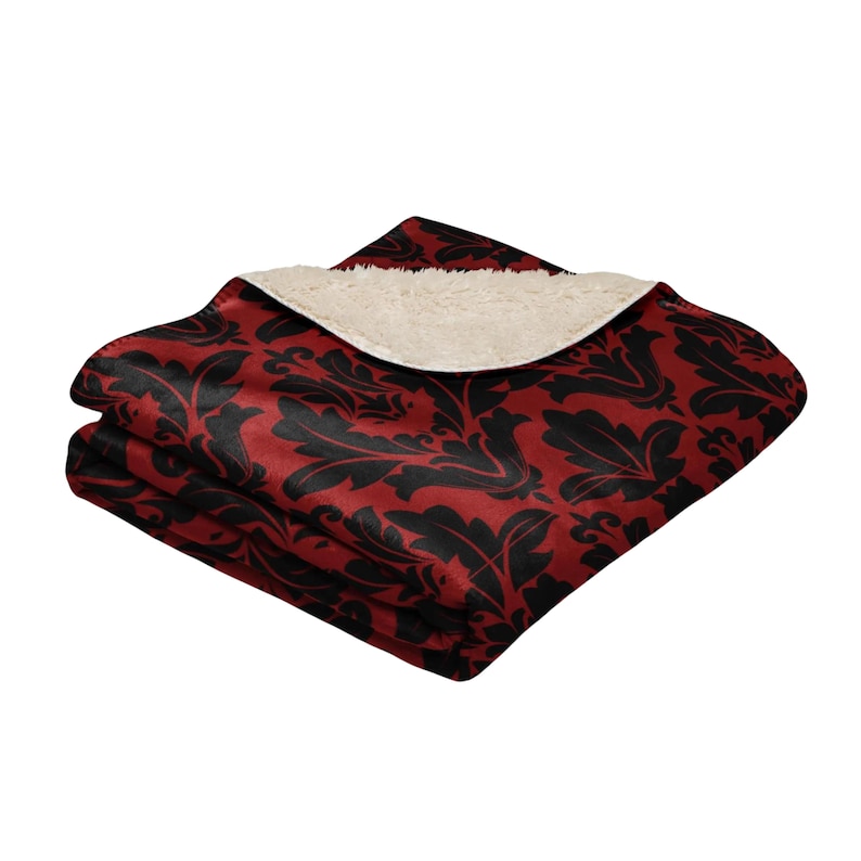 May include: A red and black patterned throw blanket with a soft, white sherpa lining. The blanket is folded in half and the sherpa lining is visible.