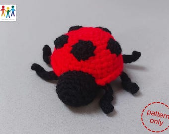 Puede incluir: Un juguete de mariquita de crochet con cuerpo rojo y manchas negras. La mariquita tiene patas y antenas negras.