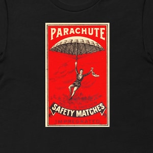 May include: Black t-shirt featuring a vintage illustration of a person parachuting from a red and white box with the text "PARACHUTE SAFETY MATCHES IMPREGRATED".
