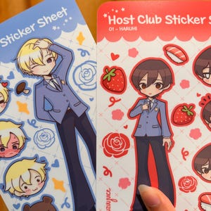 K&ouml;nnte beinhalten: Zwei Stickerb&ouml;gen mit Illustrationen im Anime-Stil. Einer ist blau mit einer blonden Figur und dem Text "Sticker Sheet". Der andere ist rot mit einer braunhaarigen Figur und dem Text "Host Club Sticker S". Beide B&ouml;gen haben zus&auml;tzliche Charakterillustrationen und dekorative Elemente.