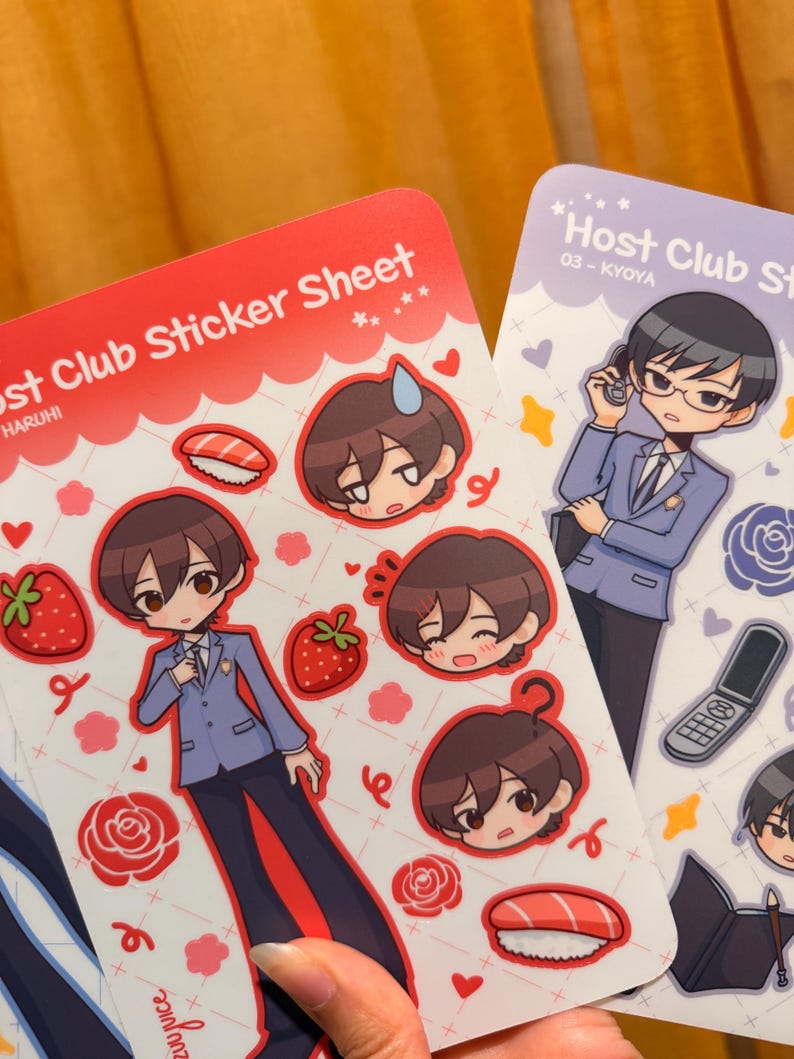 K&ouml;nnte beinhalten: Zwei Stickerb&ouml;gen mit Illustrationen im Anime-Stil. Ein rotes Blatt zeigt eine Figur in einem blauen Blazer, Erdbeeren, Sushi und Gesichter von Charakteren. Das andere ist lila und zeigt eine Figur im Anzug mit einem Telefon.