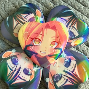 May include: Five heart-shaped anime character buttons. The central button features a character with pink hair and a smiling face. The surrounding buttons have a similar design with different hair colors and expressions. The buttons have a holographic sheen.