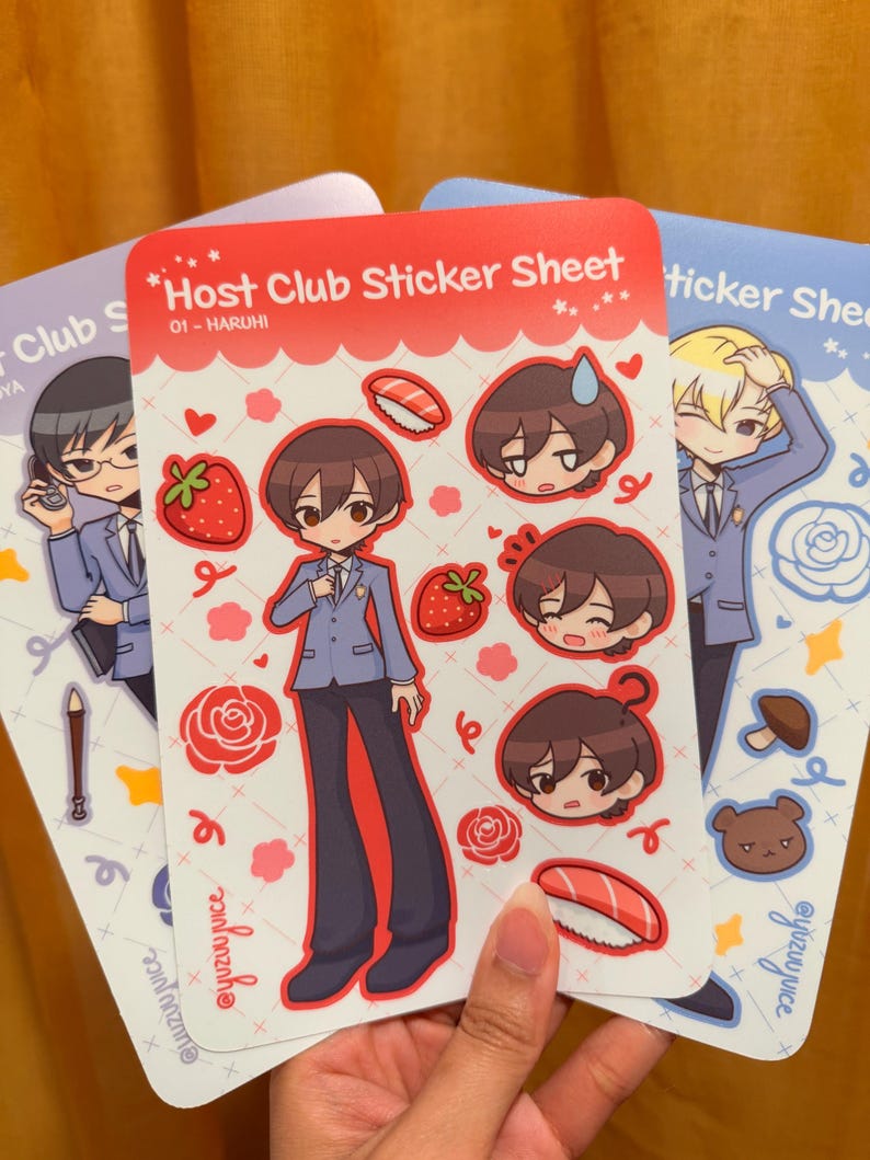 K&ouml;nnte beinhalten: Drei Stickerb&ouml;gen mit Illustrationen im Anime-Stil. Das zentrale Blatt ist rot und zeigt den Text "Host Club Sticker Sheet" und "01 - HARUHI". Die Aufkleber zeigen Charakterportr&auml;ts, Erdbeeren und Sushi.