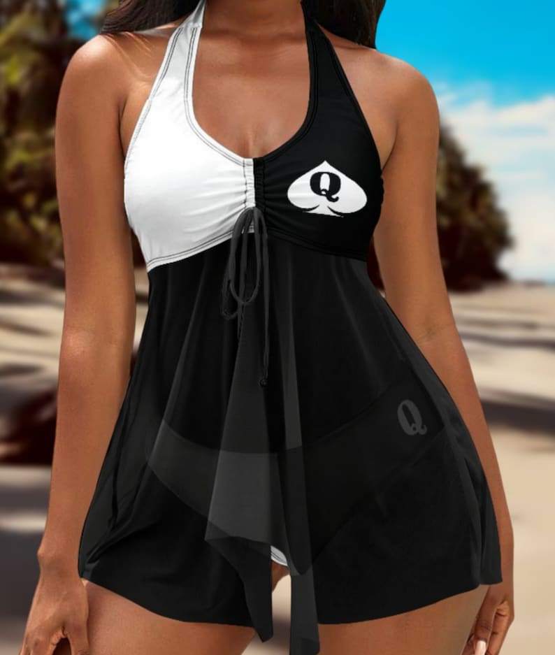 May include: Black and white halter swimsuit with a queen of hearts design. The swimsuit has a gathered detail at the waist and a ruffled hem.