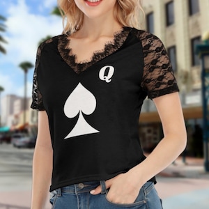 May include: Black short-sleeved shirt with a white spade and the letter Q on the front. The shirt has lace detailing on the sleeves and neckline.