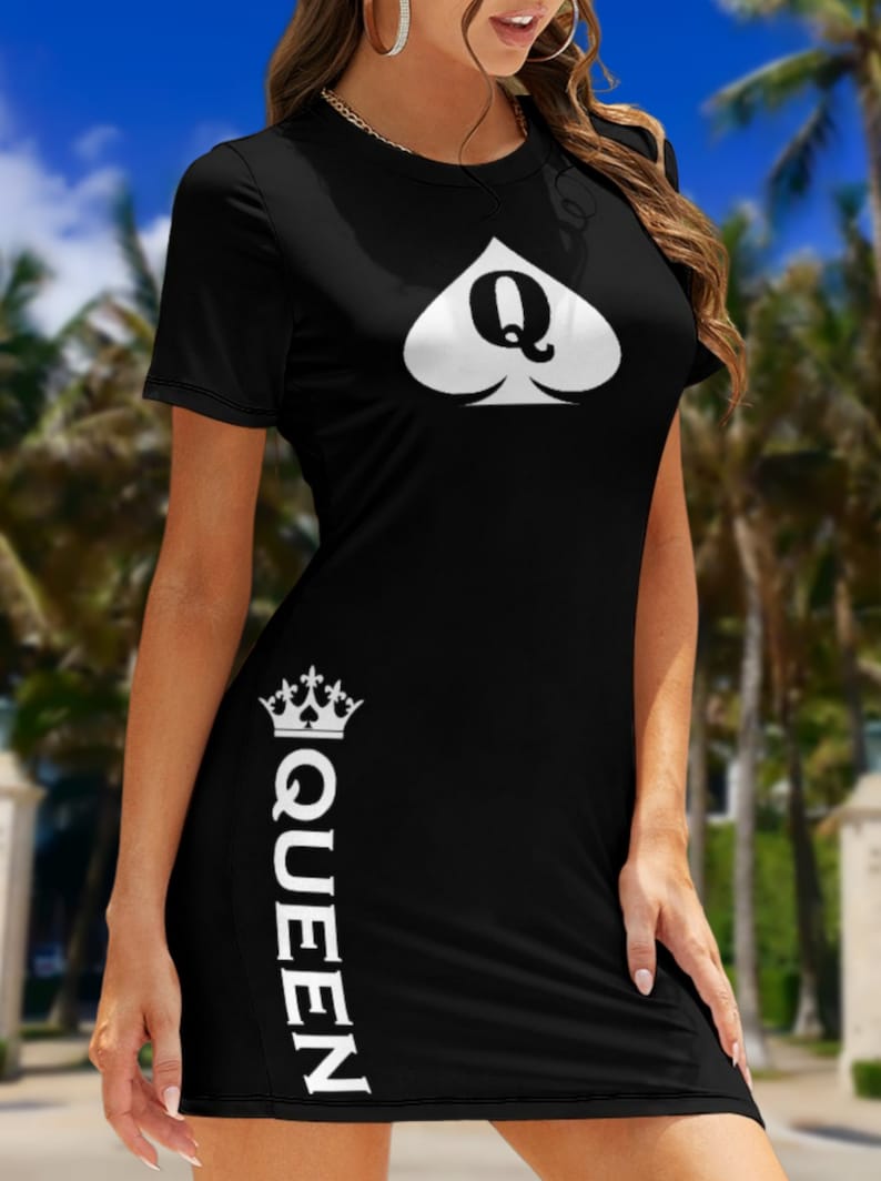 May include: A black short-sleeved dress featuring a white spade symbol with the letter Q inside on the chest. The word QUEEN is printed vertically in white along the lower right side, topped with a small white crown graphic above the text.