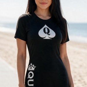 May include: A black t-shirt dress featuring a white spade symbol with the letter Q in the center on the chest. The word QUEEN is printed vertically in white along the right side, topped with a small crown graphic above the letter Q.