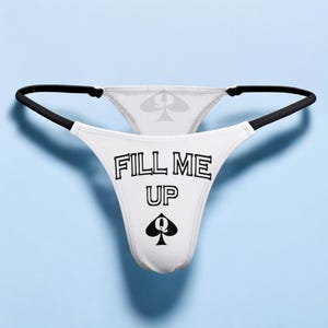 Op de afbeelding: Witte kanten string met zwarte bies en de tekst "FILL ME UP" en een schoppen koningin symbool.