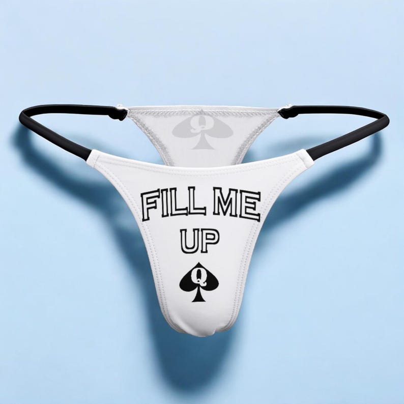 Op de afbeelding: Witte kanten string met zwarte bies en de tekst "FILL ME UP" en een schoppen koningin symbool.