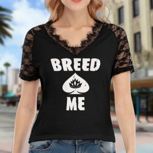 May include: Black t-shirt with lace sleeves featuring the text "BREED ME" and a stylized spade with a crown inside.