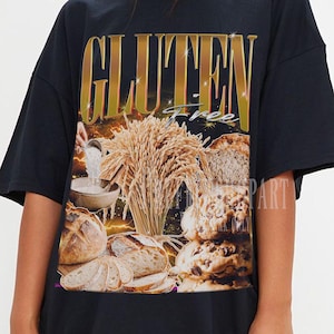 May include: Black t-shirt with a gold-coloured "GLUTEN" text and a graphic of bread and wheat. The shirt has a loose fit. The word "free" is also visible.