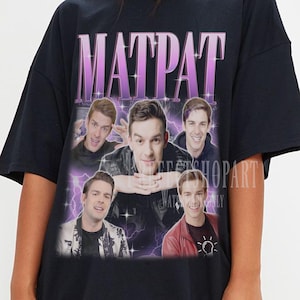 Op de afbeelding: Zwart oversized T-shirt met een grafische print van een mannengezicht en de tekst "MATPAT" in roze. De grafiek is omringd door paarse bliksemschichten en sterren.