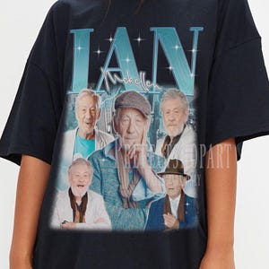 May include: Black t-shirt featuring a vintage-style graphic of several older men, with the name "IAN" in large, light blue letters at the top. The graphic has a faded, retro aesthetic.